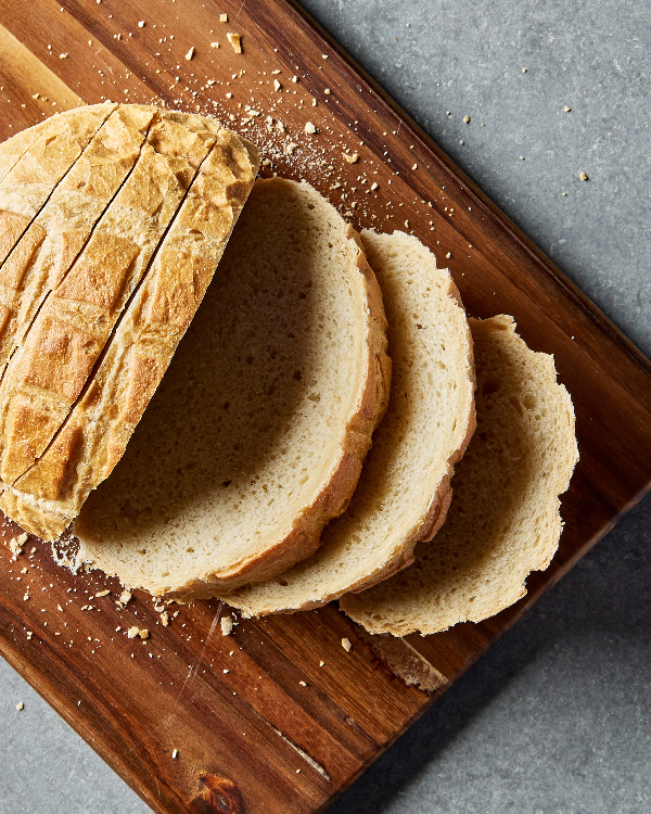 A loaf of sweet sourdough bread cut into slices on a wooden cutting board.