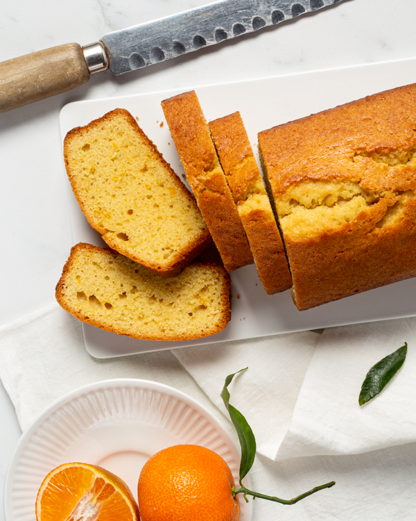 range pound cake on a platter with 4 slices cut, with a knife and oranges