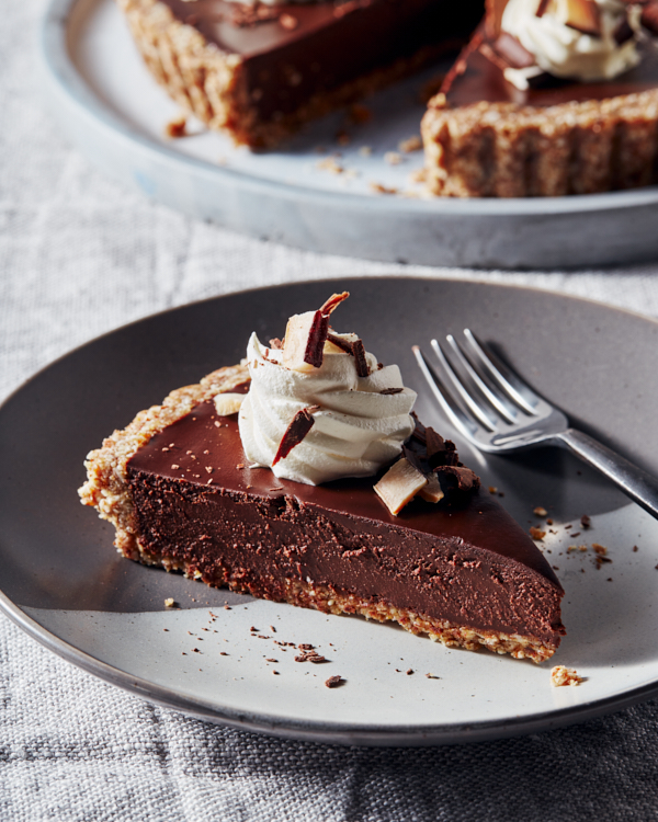 Slice of no-bake vegan chai chocolate tart on a blue-grey plate with a fork