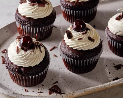 Five Black Forest cupcakes with chantilly icing topped with cherries and shaved chocolate on a platter.