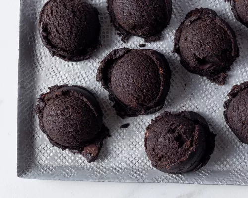 Ten scoops of edible dark chocolate cookie dough on a white tray