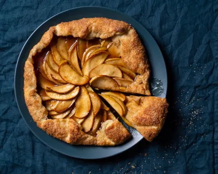 Baked apple galette with one slice cut on a blue plate on a tablecloth