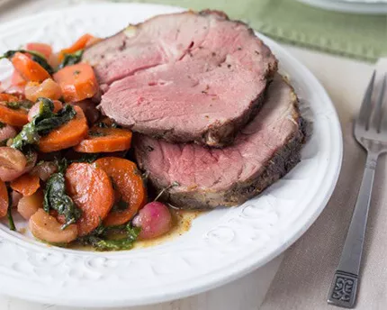 White plate with two slices of mint glazed lamb and candied vegetables